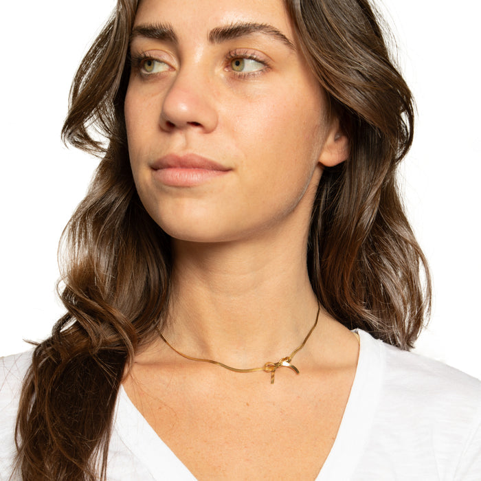 A woman wearing a white V-neck t-shirt with a mini bow necklace in gold-tone metal.