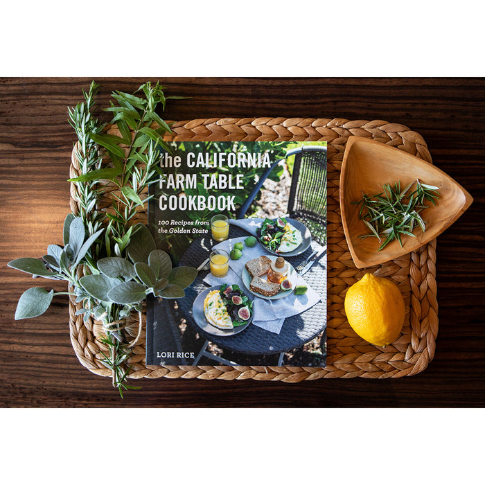 The California Farm Table Cookbook on a wood surface with herbs and a lemon