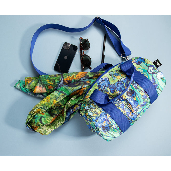 Irises bag spilling out an irises scarf, cell phone, pen and sunglasses on a blue background
